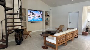Ein modernes Wohnzimmer mit einer Holztreppe, einem großen Flachbildfernseher, einer Couch und einem Esstisch.