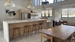 Una cocina moderna con una isla central, taburetes de bar, una mesa de comedor e iluminación colgante.