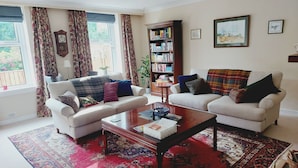 A living room with two white sofas, a coffee table, a bookshelf, and a large window with curtains. - ISLAY House, Comfortable home- private garden, in quiet village, near Edinburgh (Pencaitland)
