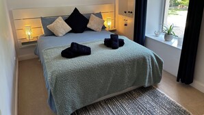 A neatly made bed with a blue blanket, two black towels, and a framed picture above it. - ISLAY House, Comfortable home- private garden, in quiet village, near Edinburgh (Pencaitland)