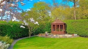 A gazebo in a well-maintained garden with a circular stone pathway, surrounded by lush greenery and flowering trees. - ISLAY House, Comfortable home- private garden, in quiet village, near Edinburgh (Pencaitland)