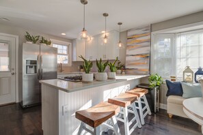 Une cuisine moderne dotée d’un îlot central, de tabourets de bar et de luminaires suspendus.