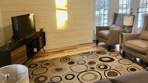 A living room with a flat-screen TV, two armchairs, a lamp, and a patterned rug.