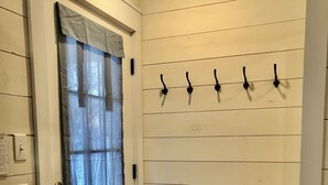 A room with a door, a wall-mounted coat rack, a basket, and a checkered doormat.