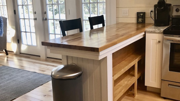 A kitchen with a wooden island, white cabinets, and a stainless steel trash can.