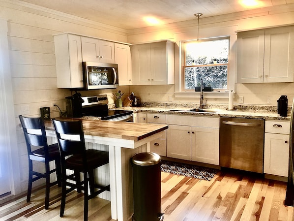 A kitchen with white cabinets, a microwave, a sink, and a window.