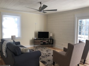 A living room with a ceiling fan, a TV on a stand, a sofa, a chair, and a patterned rug.