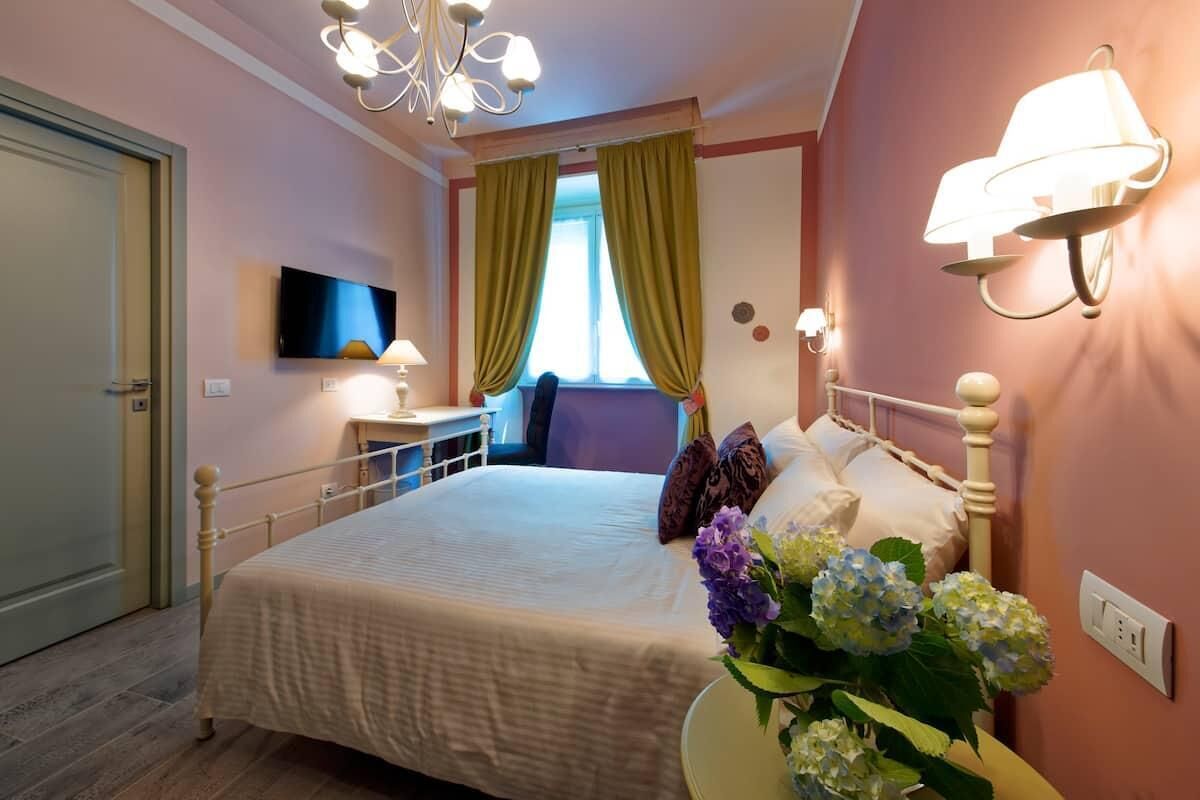 A bedroom with a bed, a bedside table, a TV, and a wall-mounted lamp.