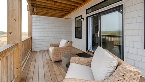 Une terrasse en bois, meublée de meubles en osier, et une porte vitrée donnant sur un espace extérieur.