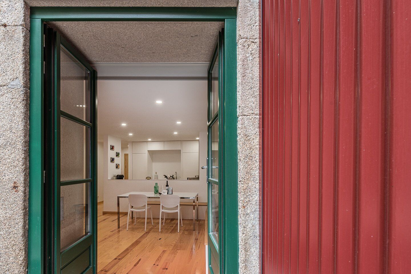 Una cocina moderna con zona de comedor, piso de madera y pared exterior roja.