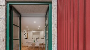 A modern kitchen with a dining area, wooden flooring, and a red exterior wall. - GuestReady - Green Bay Garden (Porto)
