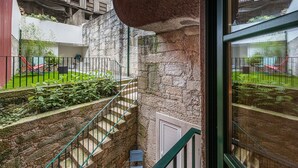 A courtyard with a stone wall, a metal staircase, and a view of a building with balconies. - GuestReady - Green Bay Garden (Porto)