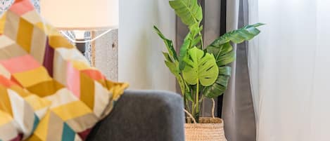 Una sala de estar acogedora con un sofá gris, una manta de colores, una planta de Monstera en maceta y una lámpara.