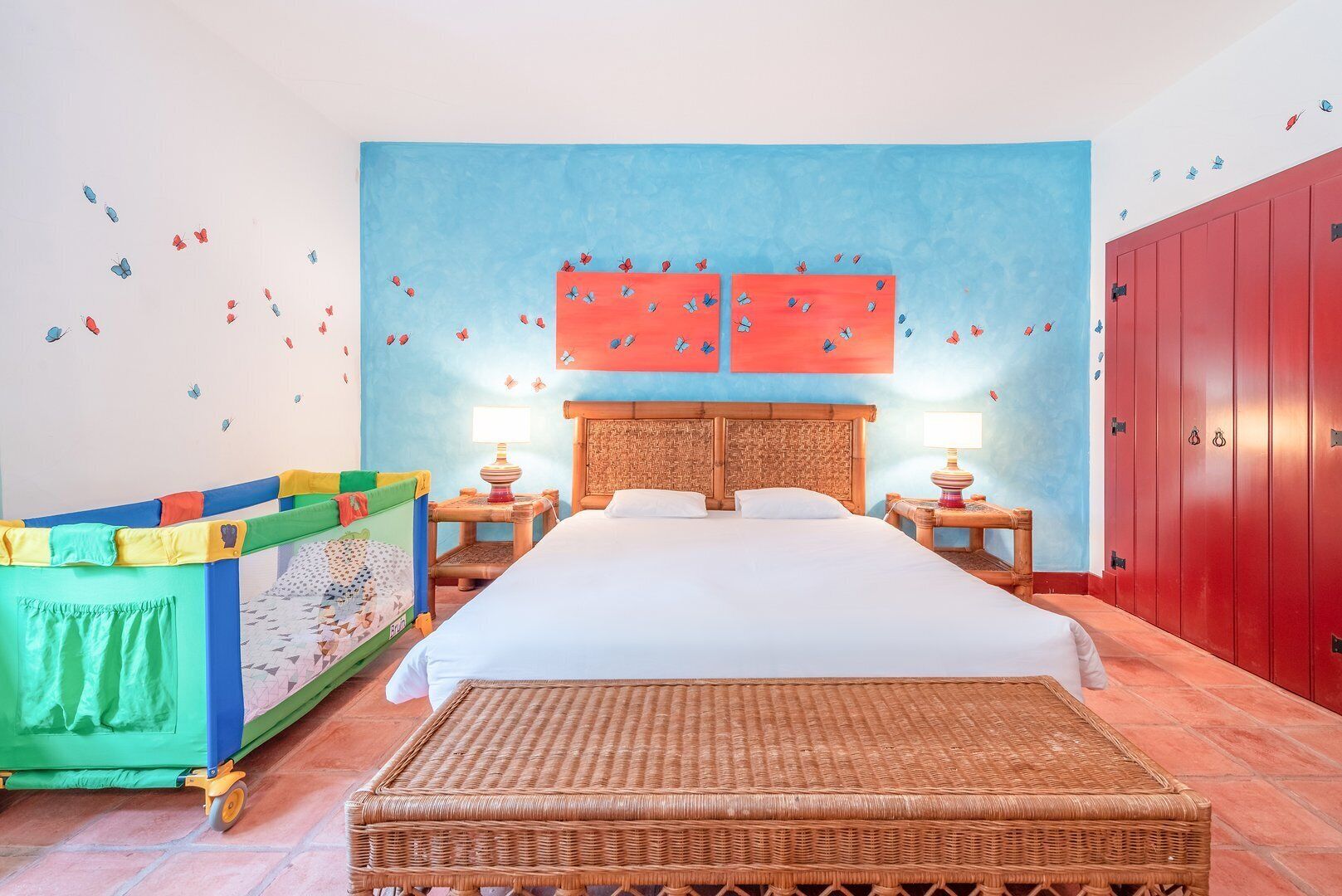 A room with a bed, two nightstands, a green playpen, and red lockers.