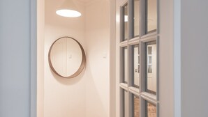 A hallway with a round mirror on the wall, a hanging light fixture, and a door with multiple windows.