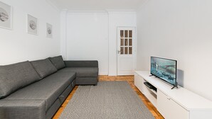A modern living room with a grey sectional sofa, a flat-screen TV on a white stand, and a small rug on a wooden floor.
