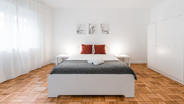 A modern bedroom with a white bed, red pillows, a grey blanket, and a white wardrobe.