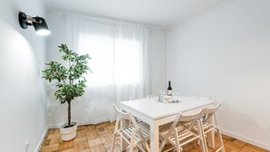 A white dining table with four chairs, a potted plant, a bottle of wine, and a glass on the table.
