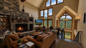 A spacious living room with a stone fireplace, leather sofa, and a large TV. - Purgatory Cabin with Views and Hot Tub (Durango)