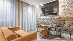 Une chambre moderne avec un mur en pierre, un téléviseur fixé au mur, un canapé et une petite table ronde.