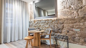 Une pièce chaleureuse avec un mur en pierre, une table en bois avec des chaises, un miroir et une fenêtre avec des rideaux.