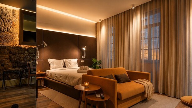 Une chambre moderne avec un lit, un canapé, une petite table et un mur en pierre.