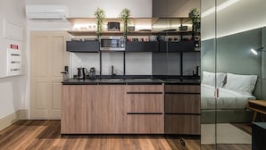 Une cuisine moderne dotée d’un îlot central, d’appareils électroménagers intégrés et d’une cloison en verre qui la sépare d’une chambre à coucher.