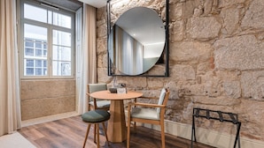 Une pièce avec un mur en pierre, une table ronde en bois accompagnée de deux chaises, un miroir et une fenêtre avec des rideaux.