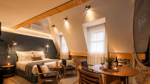 A modern bedroom with a bed, bedside tables, a round dining table, and a stone accent wall. - GuestReady - Mercadores Apartments - Room G (Porto)