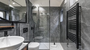 Une salle de bain moderne avec une douche à parois de verre, un lavabo blanc et un porte-serviettes noir.