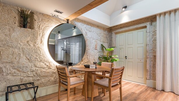 Un coin repas avec une table ronde et quatre chaises, un grand miroir, une plante en pot et un mur en pierre.