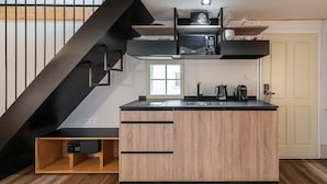 Une cuisine moderne avec un îlot central en bois, des appareils électroménagers noirs et un escalier noir.