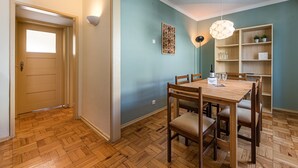 A dining area with a wooden table and chairs, a pendant light, and a bookshelf with decorative items. - GuestReady - City & Beach Garden Home (Porto)