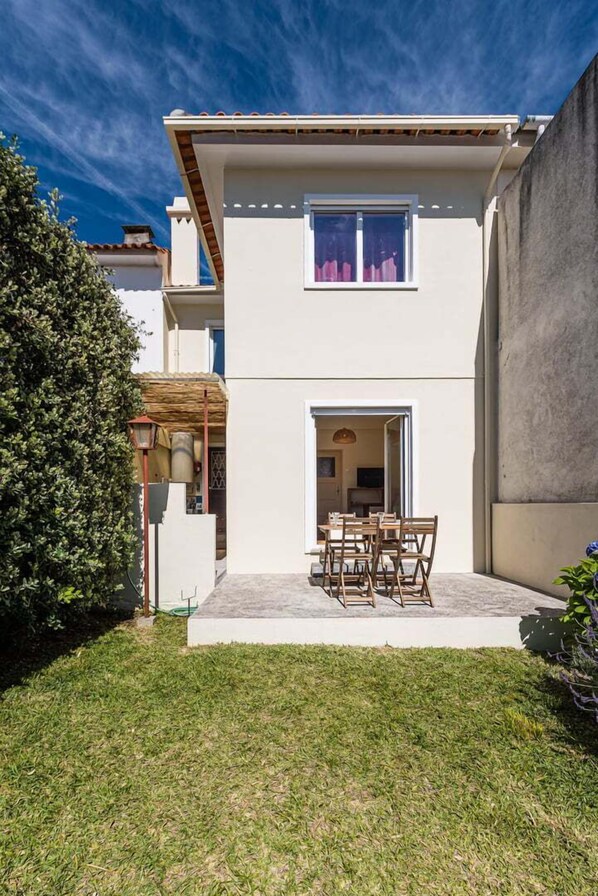 A two-story building with a flat roof, a covered patio with a table and chairs, and a well-maintained lawn.
