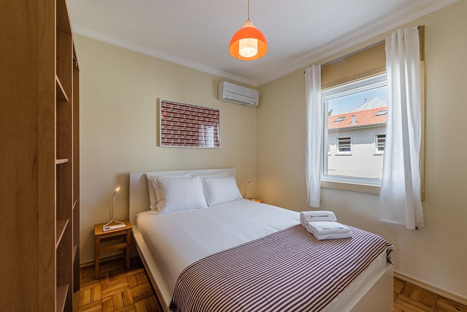 Una habitación de hotel con una cama, una mesita de noche, una ventana con cortinas y una lámpara colgante.