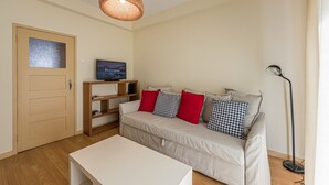 A cozy living room with a sofa, a television on a wooden stand, a white coffee table, and a floor lamp. - GuestReady - City & Beach Garden Home (Porto)