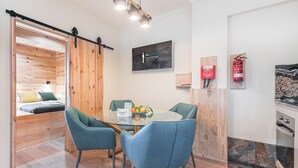 A modern kitchen with a wooden interior, a dining area with blue chairs, and a bed with a wooden headboard. - GuestReady - Contemporary cabin in Rua da Alegria (Porto)