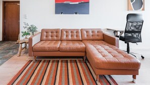 A brown leather sectional sofa with a wooden coffee table and a striped rug in a modern living room with a red abstract painting above. - GuestReady - Contemporary cabin in Rua da Alegria (Porto)