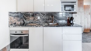 A modern kitchen with white cabinets, a black marble countertop, a built-in oven, a microwave, and a coffee machine. - GuestReady - Contemporary cabin in Rua da Alegria (Porto)