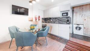 A modern kitchen with white cabinets, a black and white marble backsplash, a built-in oven, a microwave, and a washing machine. There is a dining table with two chairs and a small plant on it. - GuestReady - Contemporary cabin in Rua da Alegria (Porto)