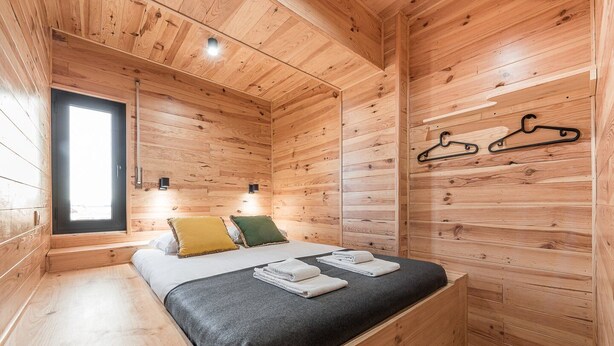 A wooden cabin room with a bed, two pillows, a window, and a wall-mounted coat rack. - GuestReady - Contemporary cabin in Rua da Alegria (Porto)