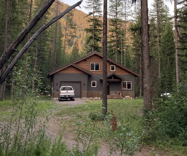 A cabin with a garage, surrounded by dense forest and mountains.