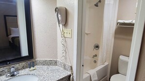 Un baño con lavamanos de encimera de granito, un espejo, ducha con puerta de vidrio y un inodoro.