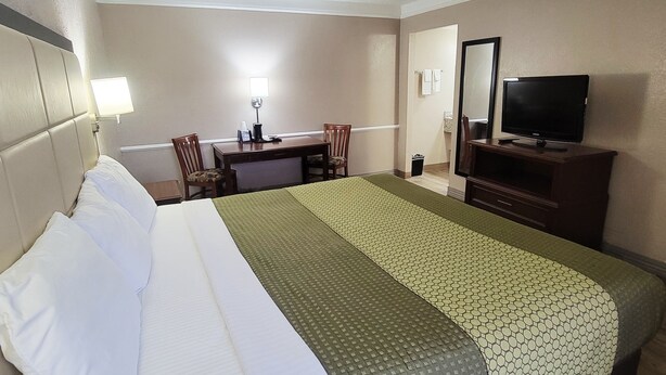 Habitación de hotel con una cama grande, un escritorio con silla, televisor sobre un mueble bajo y un espejo en la pared.