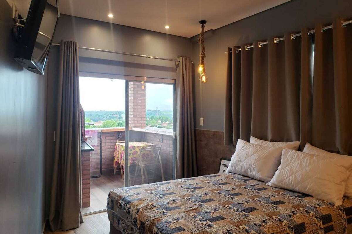 Une chambre dotée d’un grand lit, d’un téléviseur fixé au mur et d’un balcon avec une table et des chaises.