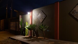 A nighttime view of a building with a textured wall, a decorative pattern, and a small potted plant on the ground. - Águas Chalés Temporada (São Pedro)