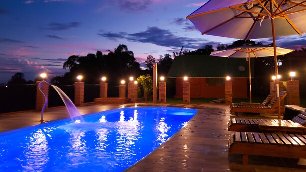 A swimming pool with a water feature, surrounded by lounge chairs and an umbrella. - Águas Chalés Temporada (São Pedro)