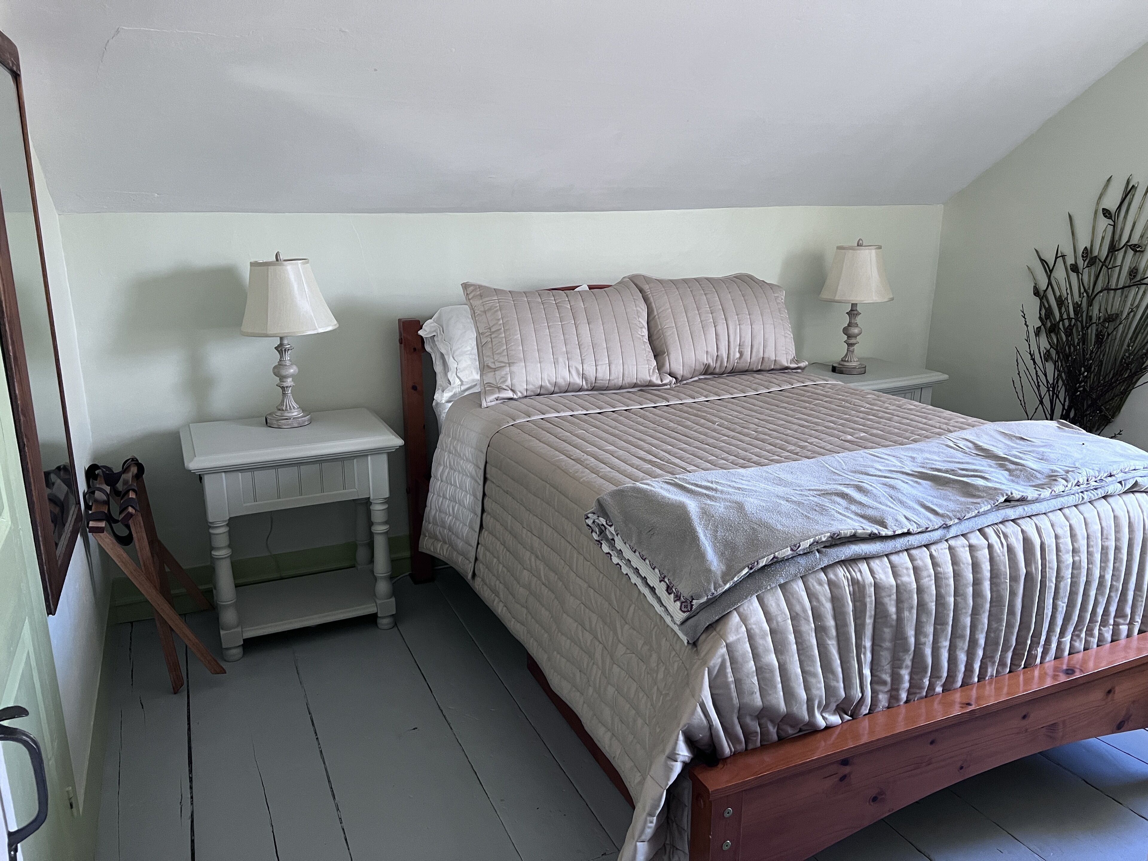 A bedroom with a wooden bed, two bedside tables with lamps, a white nightstand, and a mirror.