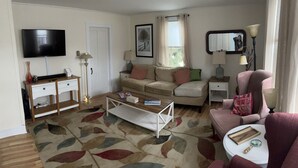 A living room with a sofa, a coffee table, a TV, and a lamp. - Charming, updated 3 bedroom farmhouse farm stay.  (Williamsburg)