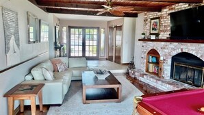A living room with a sofa, coffee table, and a pool table. There is a fireplace with a brick surround and a flat-screen TV mounted above it. - FarmStay HillTop wine country views 6BR/4BA (Paso Robles)